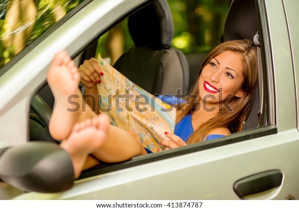 Beautiful smiling girl taking it easy in car,\
holding map and stretching her naked legs out the window of car.\
Selective focus.