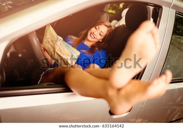 Beautiful smiling girl taking it easy in car,
holding map and stretching her naked legs out the window of car.
Selective focus.