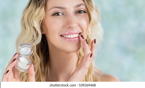 Beautiful Smiling Girl With Wavy Hair Cares Of Her Lips.  Young Blonde Woman Applying Make-up Cosmetic SPA Product. Model Using Lip Balm Or Gloss For Hydration, Nutrition, Smoothing Balm