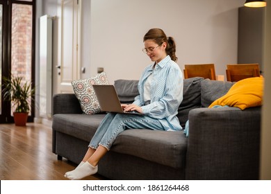 Hermosa sonriente que trabaja con una laptop sentada en el sofá en casa