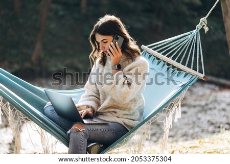 Beautiful smiling girl working with MacBook Pro in the park on a hammock