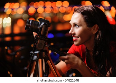 Beautiful smiling girl-photographer with camera makes night shooting in city.