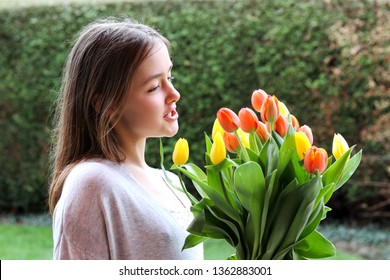 Beautiful smiling happy tween girl holding big bouquet of bright yellow and orange tulips talking to them outdoors in garden at warm spring day. Spring flowers  - Powered by Shutterstock