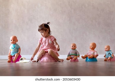 Beautiful smiling little baby sitting on potty. Cute adorable funny child girl using chamber pot together with her baby doll. Toilet training concept. Toddler learning to use the Toilet.