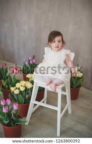 Beautiful smiling little girl in white lace dress among tulips.