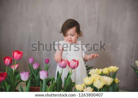 Beautiful smiling little girl in white lace dress among tulips.