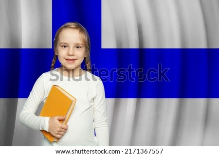 Beautiful smiling little kid with book standing against Finnish flag background