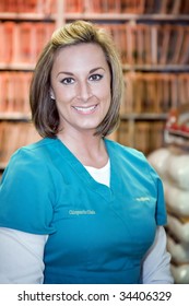 Beautiful Smiling Medical Assistant In Blue Scrubs Standing In Front Of Files In A Doctor's Office.