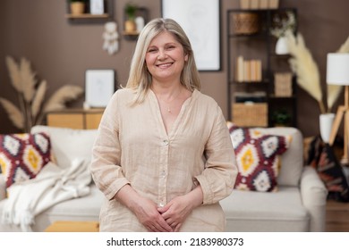 Beautiful Smiling Middle Aged Woman Portrait Of A Girl On The Background Of Warm Cozy Boho Living Room. Elegantly Dressed Older Lady.