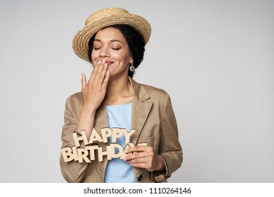 Beautiful Smiling Mixed Race Woman Holding Happy Birthday Text Excited Of Happiness With Closed Eyes Covering Her Mouth With Hand, Isolated On Gray Background