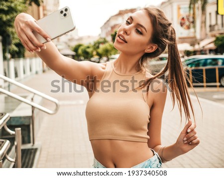Beautiful smiling model in summer casual clothes.Sexy carefree female posing in the street in sunglasses.Taking selfie self portrait photos on smartphone