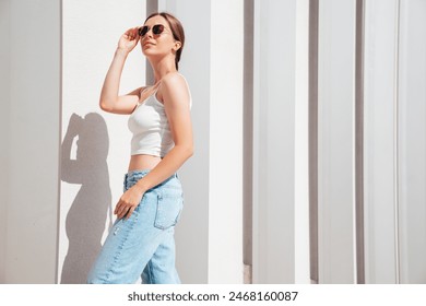 Beautiful smiling model in sunglasses. Female dressed in summer hipster white T-shirt and jeans. Posing near white wall in the street. Funny and positive woman having fun outdoors - Powered by Shutterstock