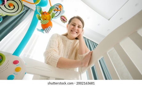 Beautiful smiling mother leaning on cradle and looking on her sleeping baby. Concept of parenting, family happiness and baby development. - Powered by Shutterstock