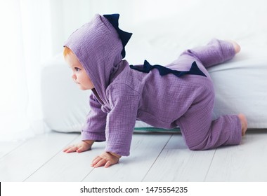 beautiful smiling, nine month old, infant baby girl in dinosaur costume, is sitting on the bed
