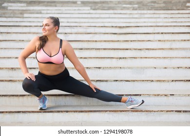 Beautiful smiling plus size girl in sporty top and leggings doing sport on stairs joyfully looking aside spending time outdoor
