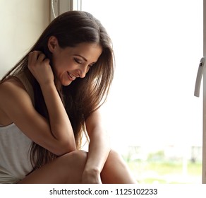 Beautiful smiling positive woman sitting near the window and looking down with pensive look. Closeup portrait - Shutterstock ID 1125102233