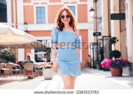 Beautiful smiling redhead model. Trendy female posing in the street background. Funny and positive woman having fun outdoors. At sunny day. In top and skirt clothes and sunglasses