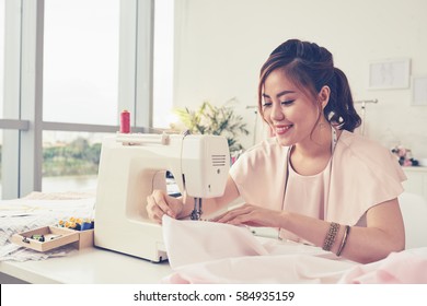 Beautiful smiling tailor enjoying work on sewing machine