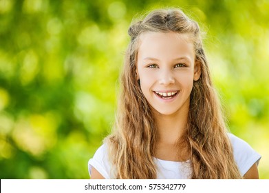 Schönes lächelndes Teenagermädchen in weißer Bluse, auf Grün des Sommerparks.