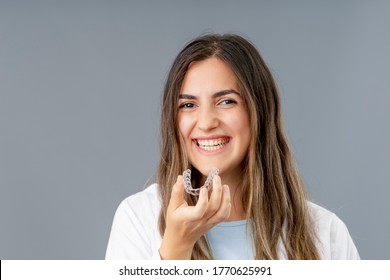 Beautiful smiling Turkish woman is holding an invisalign bracer in a grey background studio with copy space