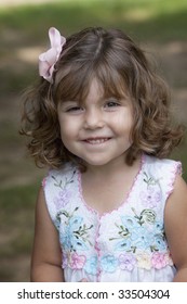 Beautiful Smiling Winking  Little Three-year-old Girl With Bouncy Natural Curly Hair Held Back With A Pink Bow.