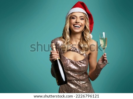 beautiful smiling woman in christmas hat and sparkle dress holding champagne glass while standing isolated