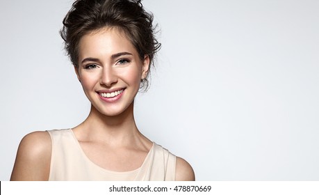 Beautiful smiling woman with clean skin, natural make-up, and white teeth on grey background