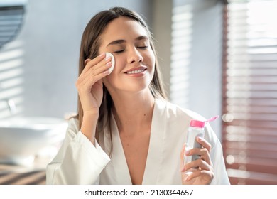 Beautiful Smiling Woman Cleansing Skin With Micellar Water And Cotton Pad While Making Daily Beauty Routine In Bathroom, Attractive Young Female Enjoying Home Skincare Treatments, Copy Space - Shutterstock ID 2130344657