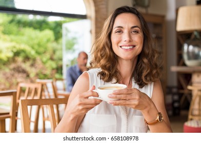 Beautiful smiling woman drinking coffee at cafe. Portrait of mature woman in a cafeteria drinking hot cappuccino and looking at camera. Pretty woman with cup of coffee. - Powered by Shutterstock