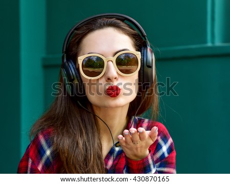 Beautiful smiling woman with headphones listens to music. Blowing lips kiss. Fashion woman in sunglasses outdoor.