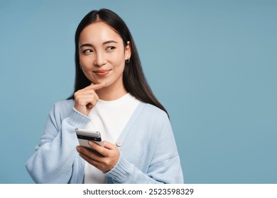 Beautiful, smiling woman holding smartphone is thinking about something, looking away isolated on blue background. Online shopping concept - Powered by Shutterstock