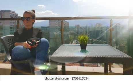 Beautiful Smiling Woman  Listening A Music With Headphones And Taking A Coffee On A Balcony With A Snowy Mountain View  In  A Sunny Morning In A City. 