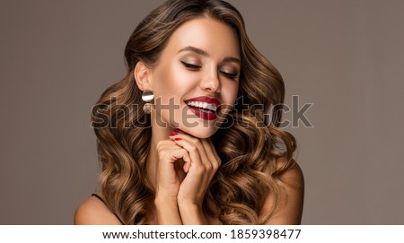 Beautiful smiling woman with long wavy hair .  Girl curly hairstyle  and red manicure nails . Beauty ,makeup and cosmetics .Smile with white and even teeth. Earring jewelry