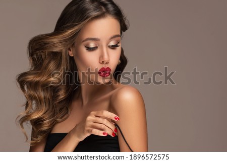Beautiful smiling woman with long wavy hair .  Girl curly hairstyle  and red manicure nails .Clothes,makeup and cosmetics . The beauty straightens the strap on the dress.