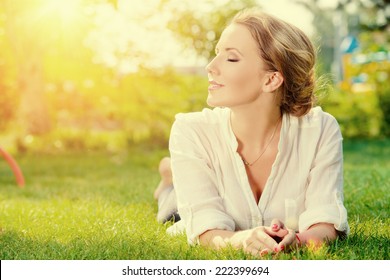 Beautiful smiling woman lying on a grass outdoor. She is absolutely happy. 