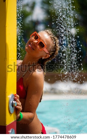 Beautiful smiling woman with pigtails standing under running water in shower in water park.