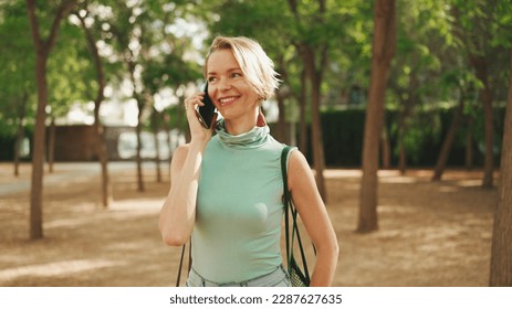 beautiful smiling woman with short blond hair in casual clothes walks through the city square, talking on cellphone - Powered by Shutterstock