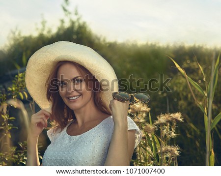 Beautiful smiling woman standing in country field in summer time during sunset. She has grass in the background that has been shot out of focus with lots of bokeh.