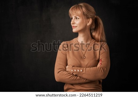 Beautiful smiling woman standing at isolated dark background. Blond haired woman wearing sweater. Copy space. Profile view.