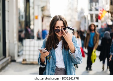 Beautiful Smiling Woman Walking On Crowded City Street From Work With Coffee Cup And Texting On Mobile Phone