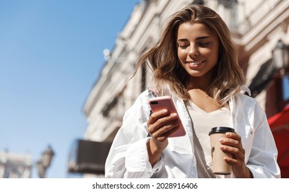 Beautiful smiling woman walking on street with coffee takeaway, chatting on mobile phone. Girl talking on smartphone on her way to meeting spot, sending message - Powered by Shutterstock