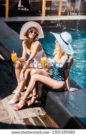beautiful smiling women sitting at poolside with cocktails
