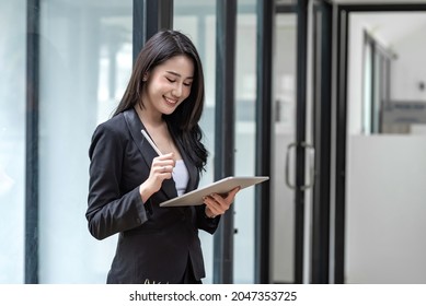 Beautiful Smiling Young Asian Businesswoman Standing Holding A Pen Using A  Tablet Happy Successful At The Office.