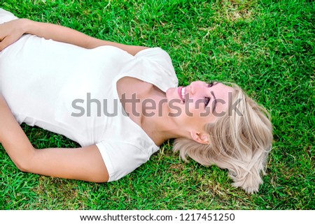 Beautiful smiling young blonde woman laying on fresh green grass in the city outdoor