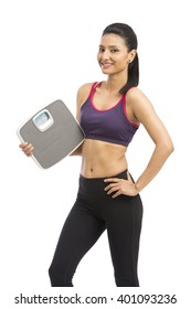 Beautiful smiling young fitness woman in tracksuit holding weighing scale over white background
