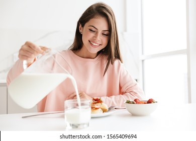 Beautiful smiling young girl having tasty healthy breakfast while sitting at the kitchen table - Powered by Shutterstock