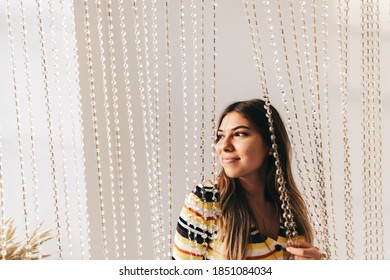 Beautiful Smiling Young Woman In Bright Living Room With White Walls And Iridescent Curtain