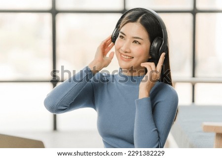 Beautiful smiling young woman in headphones chatting via laptop computer video call at home
