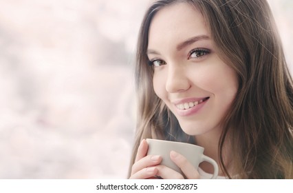 Beautiful Smiling Young Woman With Natural Make Up And Long Eyelashes Holds A Cup With Hot Coffee Or Tea. Winter Season.