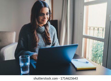 Beautiful smiling young woman sitting at home office working remotely on laptop, Positive female entrepreneur in casual clothes having video chat online at cozy office workplace, E-learning concept